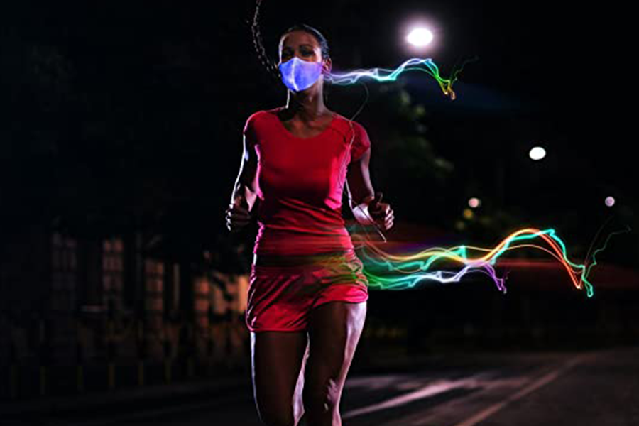 Mujer corriendo en la carretera y vistiendo traje deportivo rojo y máscara de luz LED