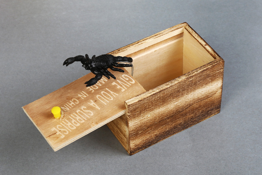 Um escorpião de plástico preto pulando de uma caixa de madeira