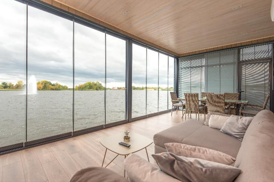 غرفة معيشة بجانب البحيرة مع نوافذ رمادية ممتدة من الأرض حتى السقف