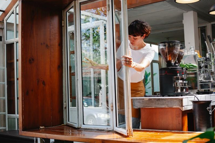 Barista at coffee shop opening a white folding window