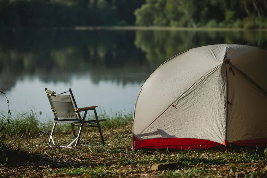 A collapsible camping chair next to a large tent