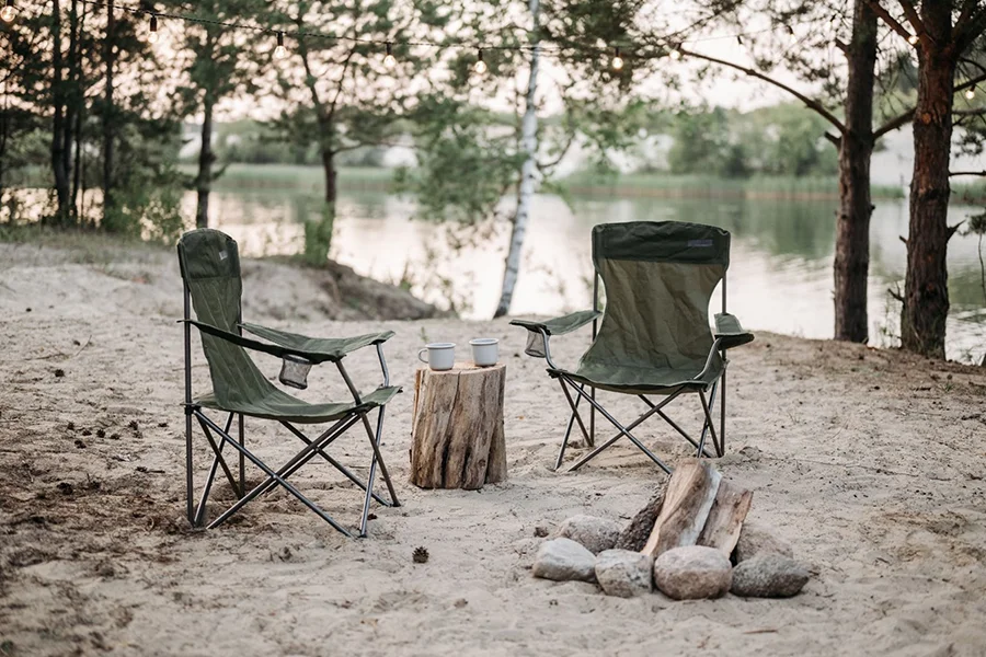 Two foldable camping chairs next to a campfire in daylight