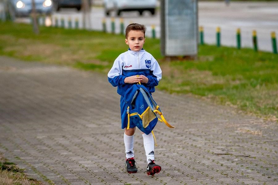 Boy wearing white and blue jacket walking on brick road