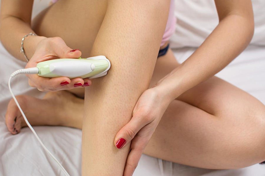 Girl using an epilator sitting on the bed