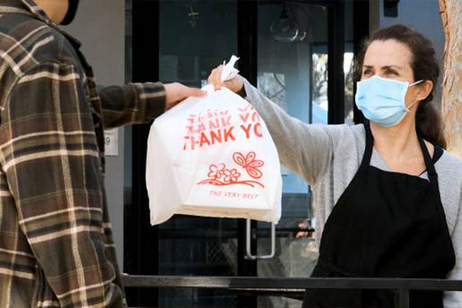 Restaurant worker handing a customer a plastic takeaway bag