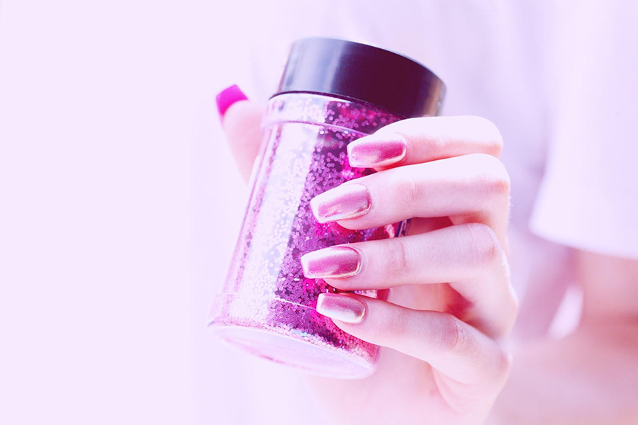 A woman holding a pink glitter nail polish