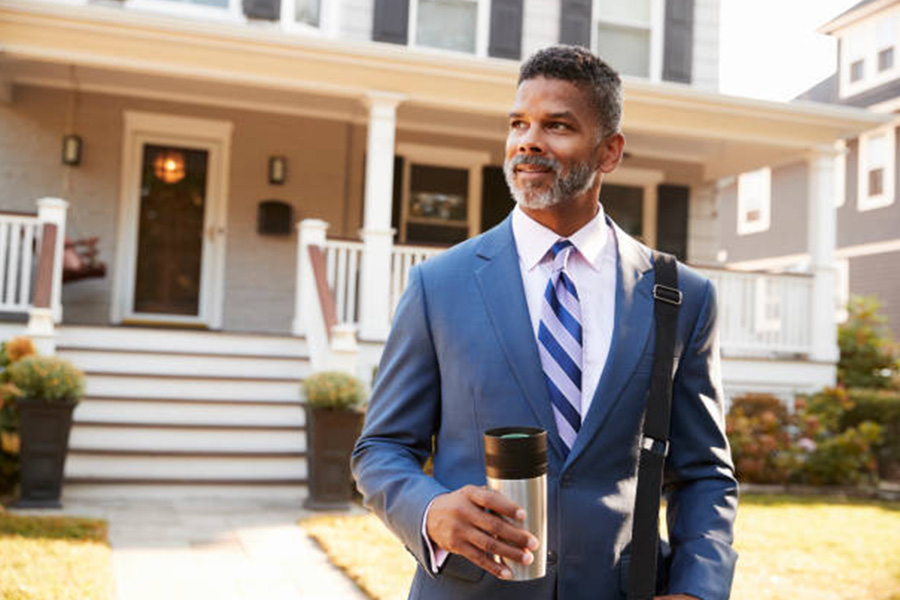 Man in suit outside house with reusable coffee cup