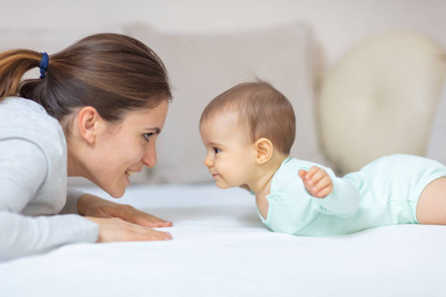 Mother on bed with child in light blue baby romper