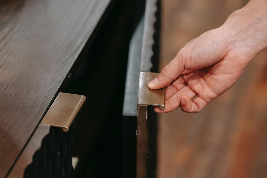 A hand opening a dark cupboard via a handle pull