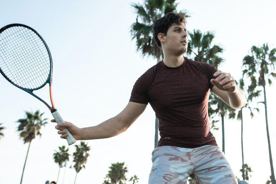 Man posing with brown tech T-shirt and tennis racket