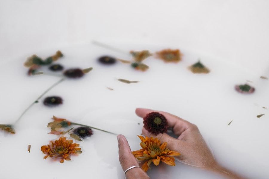 Anonymous woman holding flowers in a milky bath