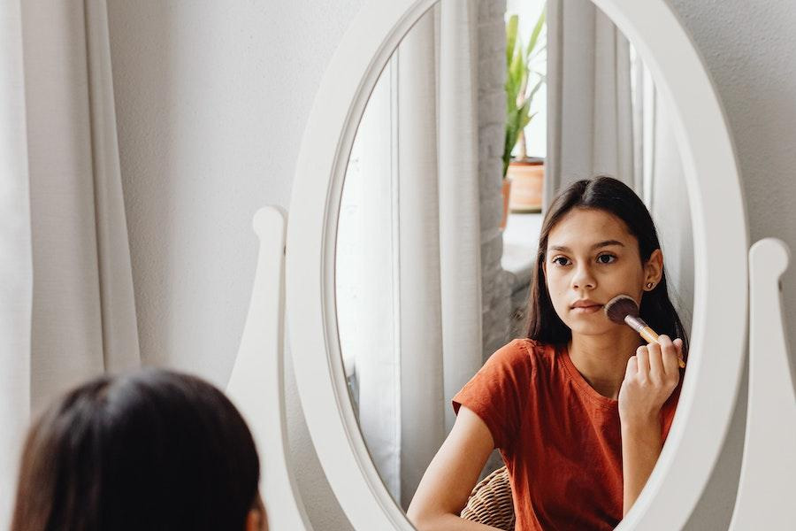 Tween applying makeup in front of a mirror