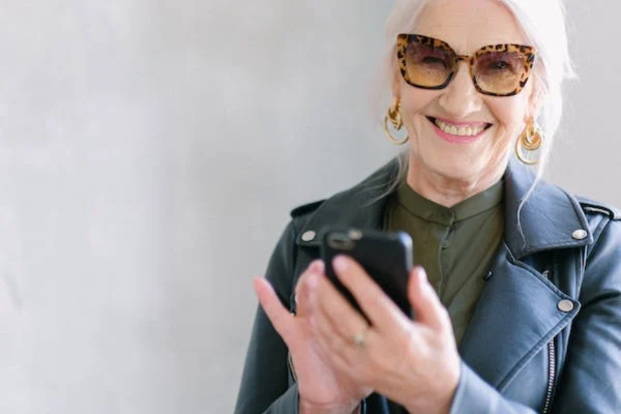 Cheerful menopaused woman using smartphone in trendy glasses