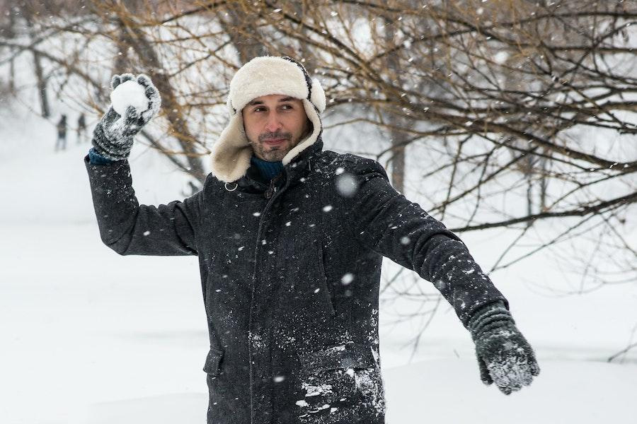 Uomo che tiene una palla di neve mentre fa oscillare un cappello da trapper