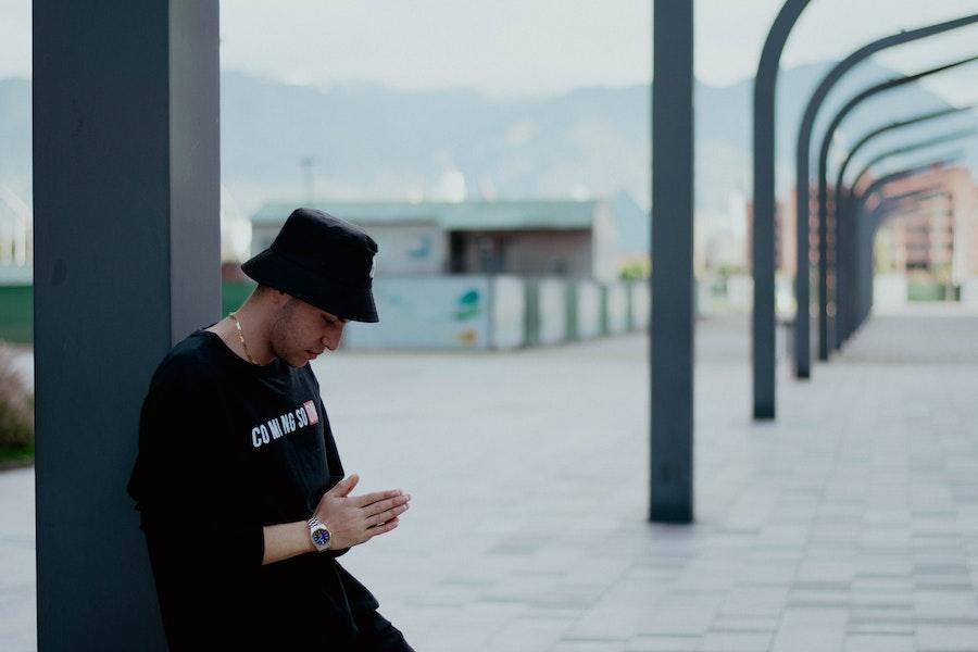 Man leaning against a pillar in a black bucket hat