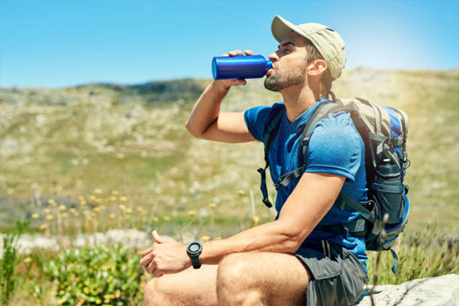 Man sitting on rock drinking water wearing a baseball cap