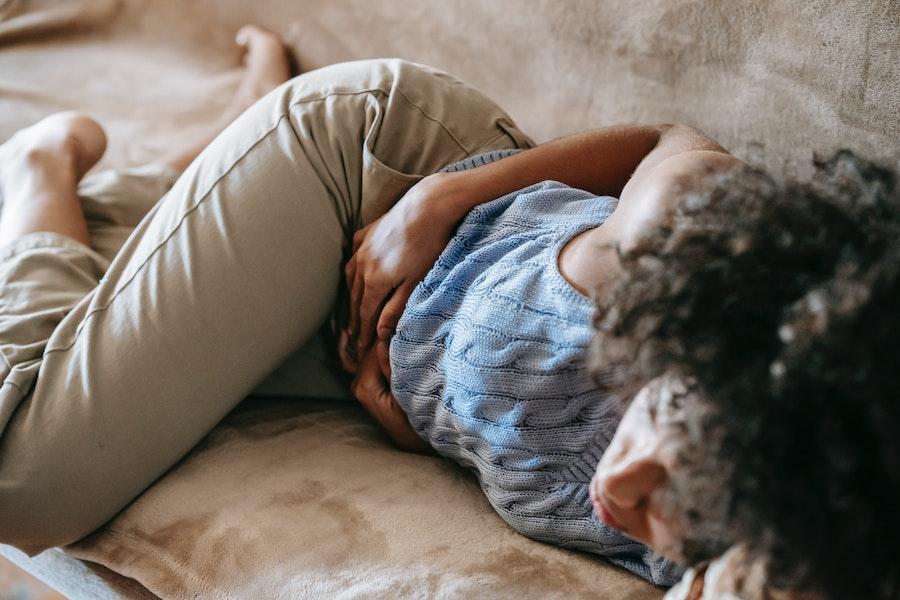 Woman lying on couch while holding her stomach in pain