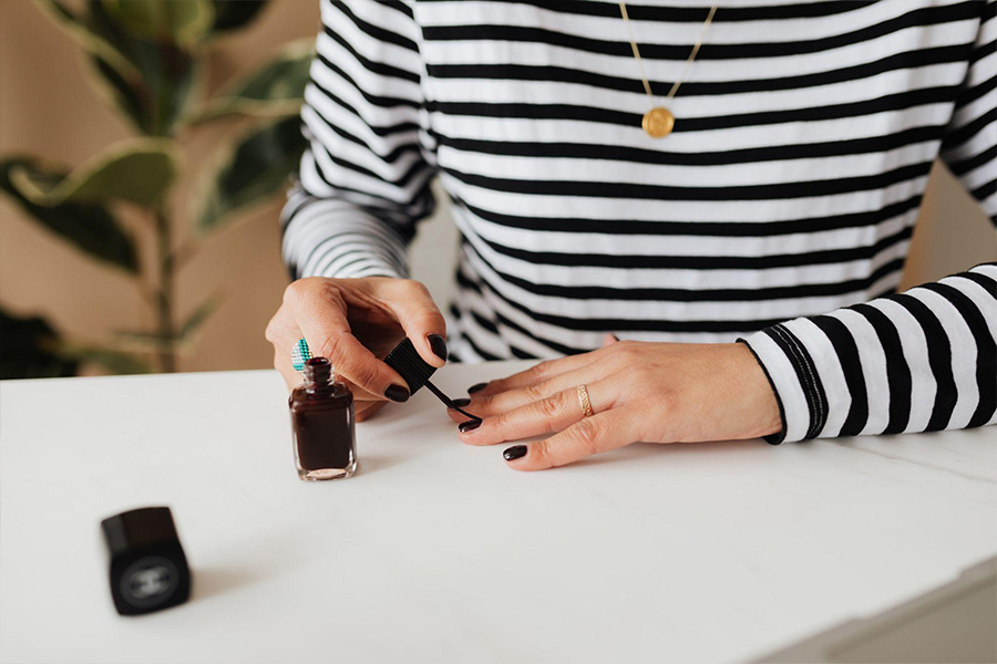 Woman painting her nails a dark color.