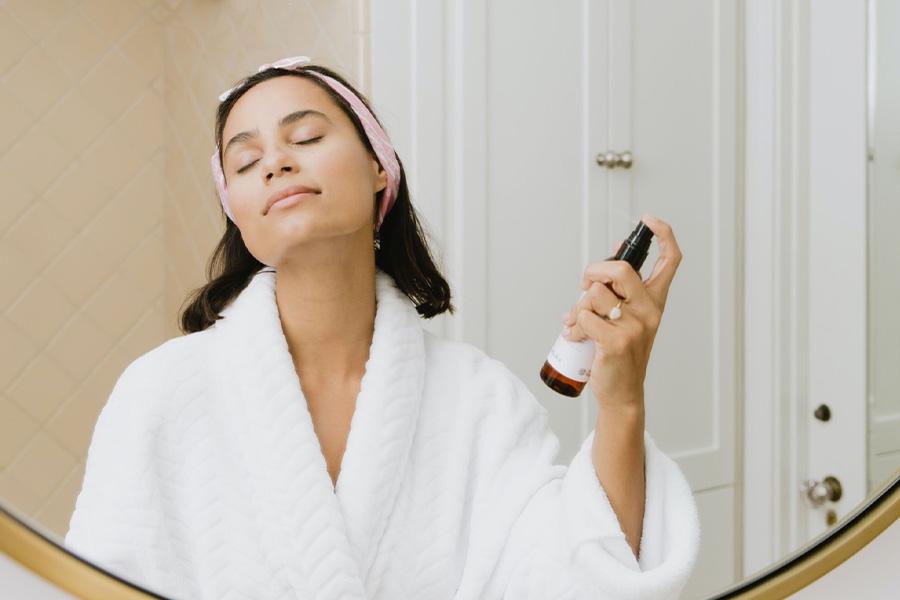 Woman spraying her face with a skincare product