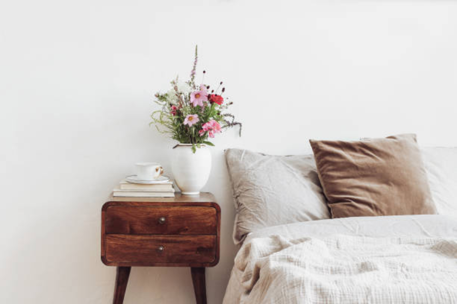 A dark wood nightstand with books and flowers on top