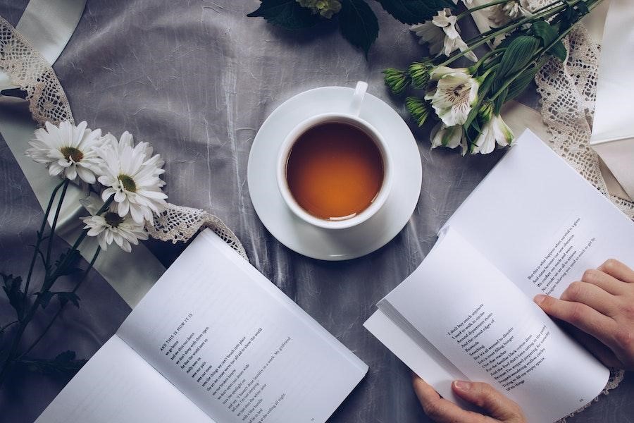 Anonymous person reading a book near a cup of coffee