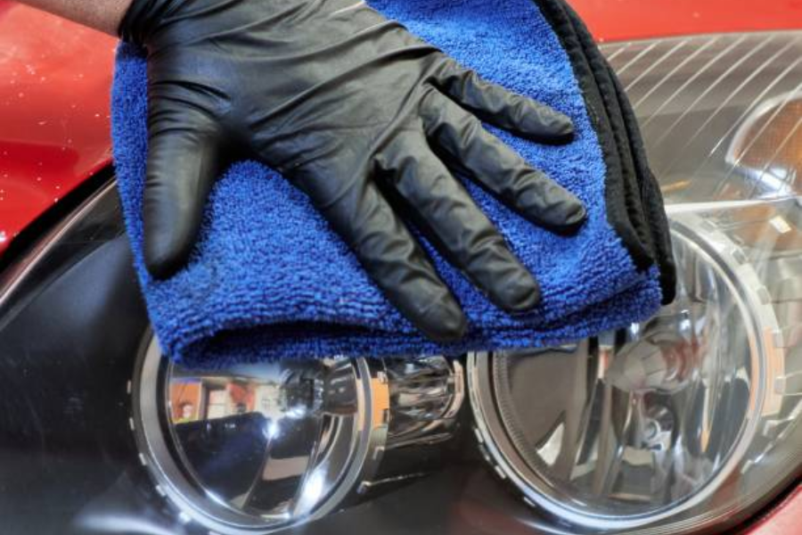 A gloved mechanic wiping a car headlight after polishing