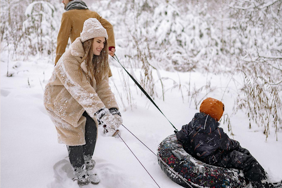 A man and woman tow a little boy in a tube across the snow