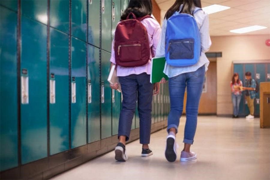 Two female high school students walking down hallway in pants