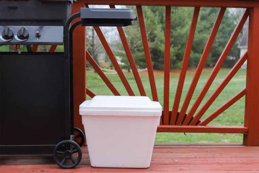 White styrofoam cooler box sitting next to an outdoor BBQ