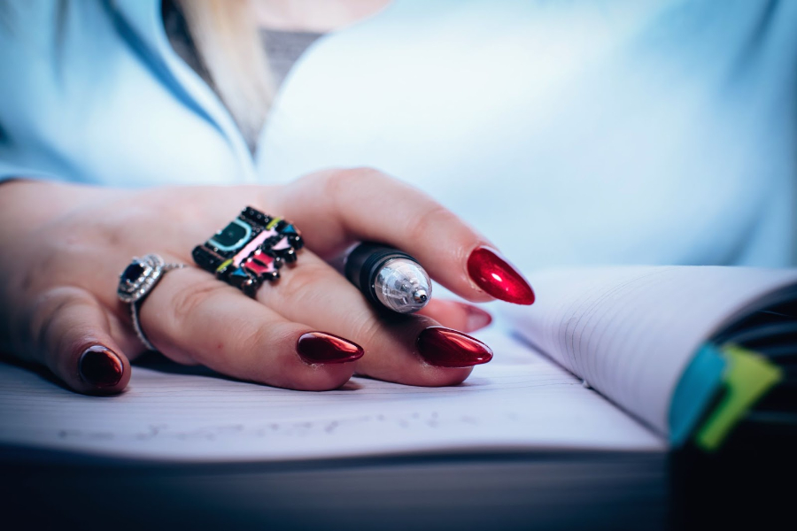 Woman holding pen and showing deep red nails