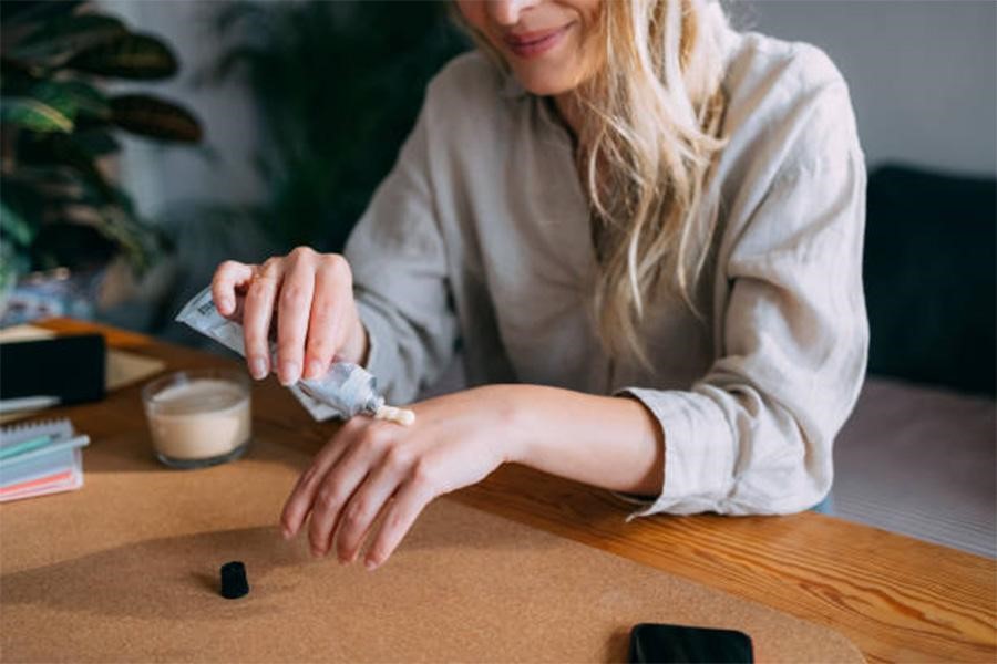 Woman sitting at desk putting cream on left hand