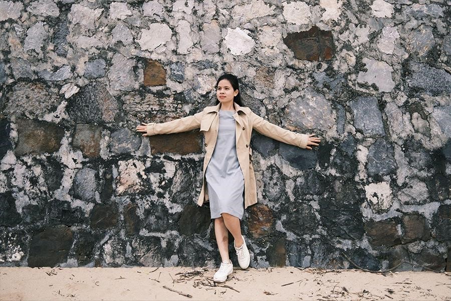 Woman wearing gray jersey dress, tan coat, and white sneakers